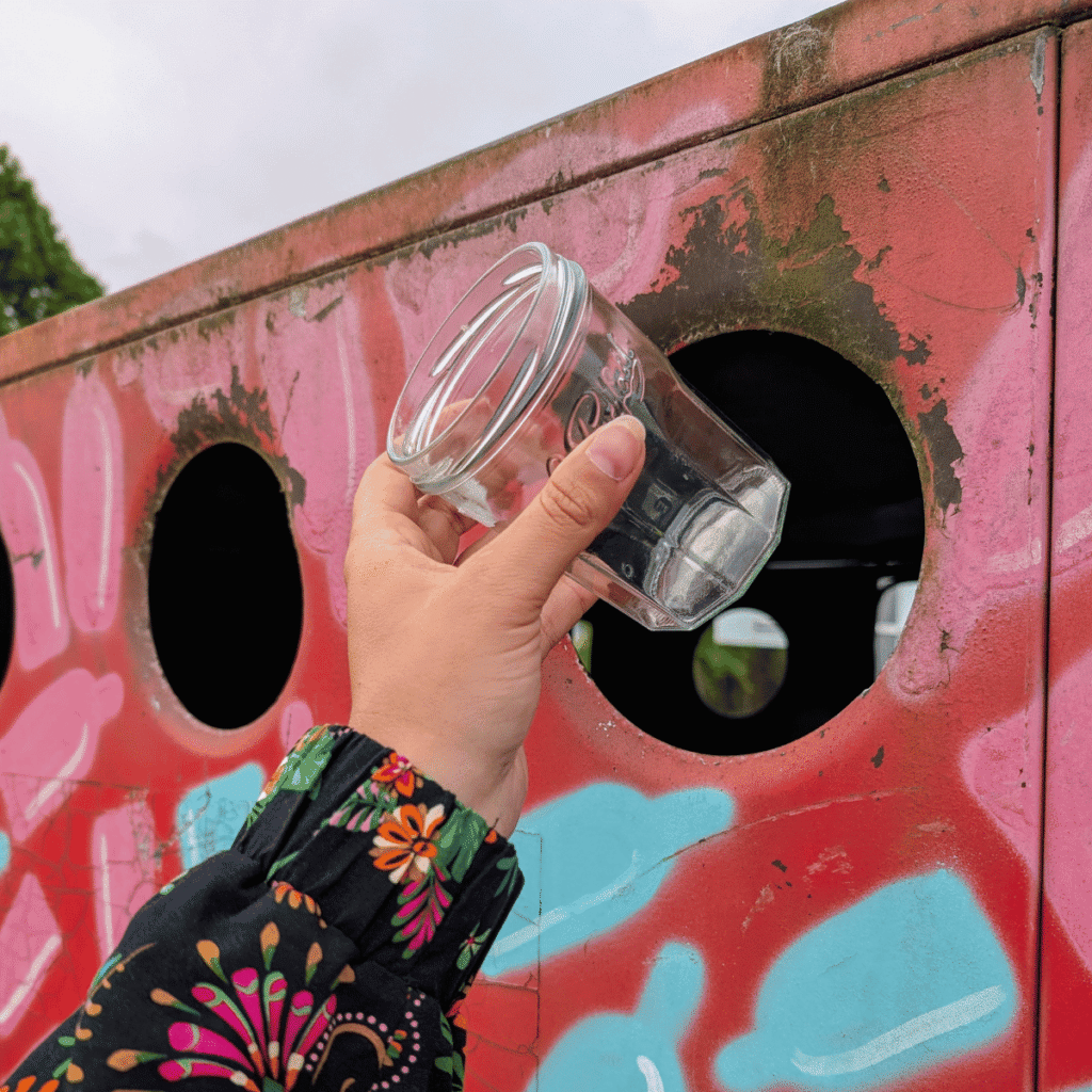 une main dépose un bocal en verre dans une colonne pour permettre son recyclage